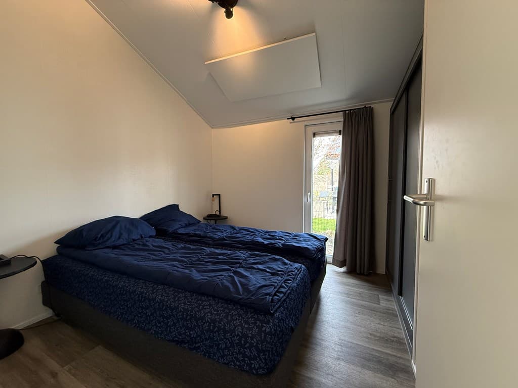Slaapkamer met twee eenpersoonsbedden, kast, nachtkastje en toegang tot een balkon via een deur met gordijnen.
