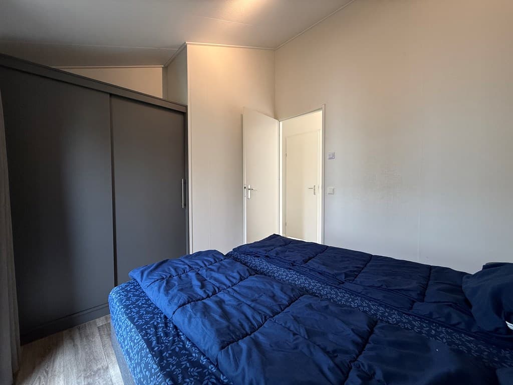 Slaapkamer met een tweepersoonsbed, een kast en een deur naar de gang.