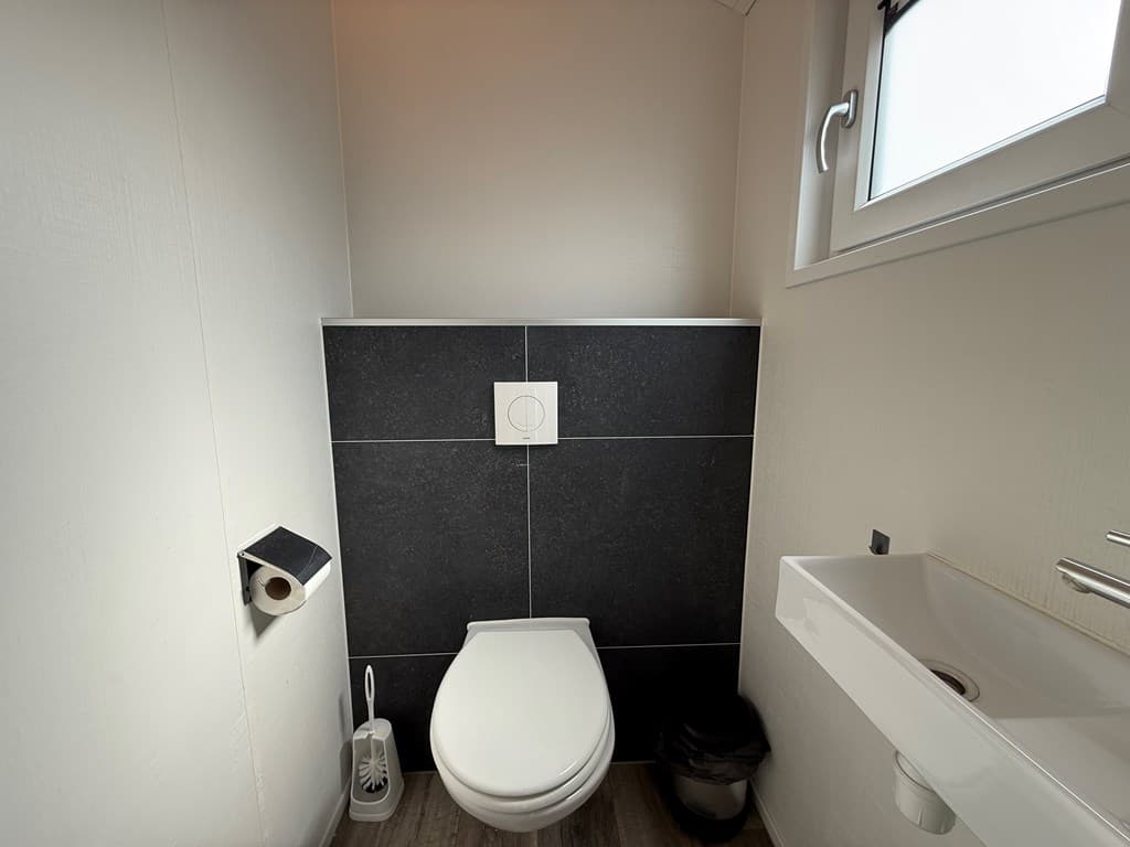 Toilet met zwart-witte wandafwerking, een wastafel en een raam voor natuurlijke verlichting.