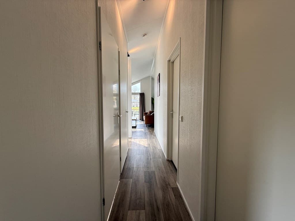 Lange gang met deuren naar verschillende kamers en veel natuurlijk licht aan het einde van de gang