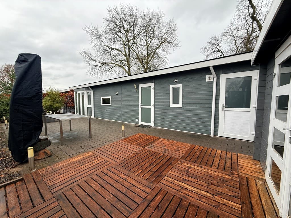 Terras van een vakantiewoning met een houten en betegelde vloer, enkele deuren en een parasol met hoes.