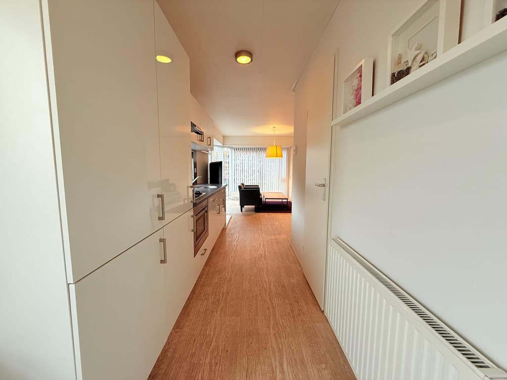 Moderne hal met lichte wanden, een keuken aan de linkerkant en een woonkamer aan het einde met een zithoek.