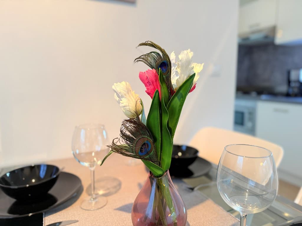 Tafelschikking met een vaas met kleurrijke bloemen, zwarte borden en glazen op een tafel in een lichte ruimte
