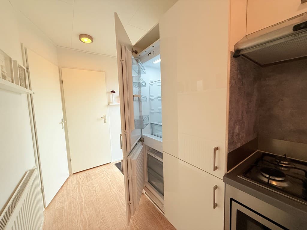 Moderne keuken met openstaande koelkast en fornuis, lichte wand en vloer in neutrale tinten.