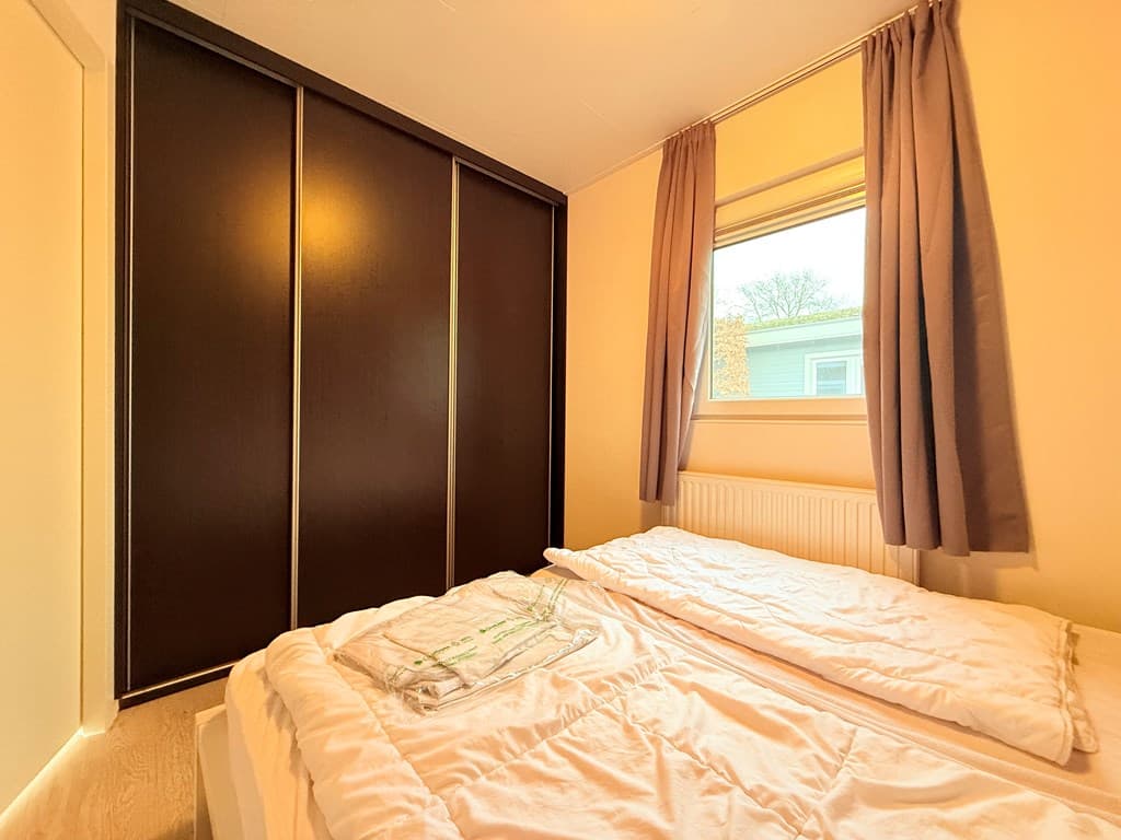 Slaapkamer met twee aparte bedden, een raam met gordijnen en een grote kast tegen de muur.