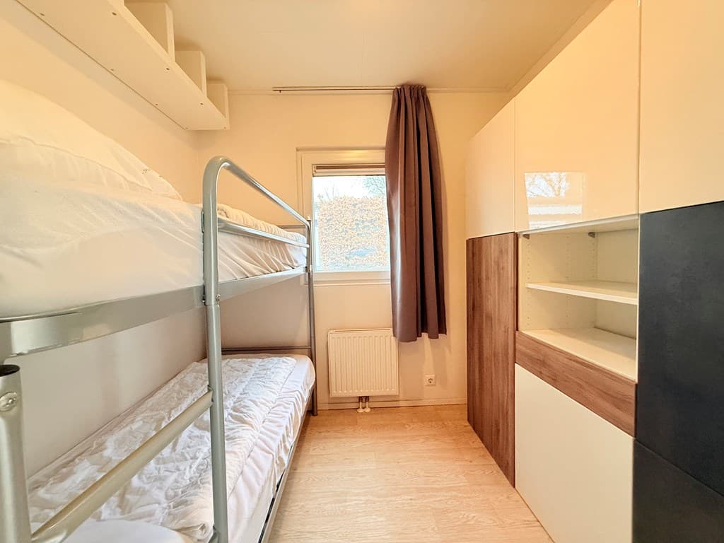 Slaapkamer met stapelbed en kast, raam met gordijn en lichte vloerbedekking