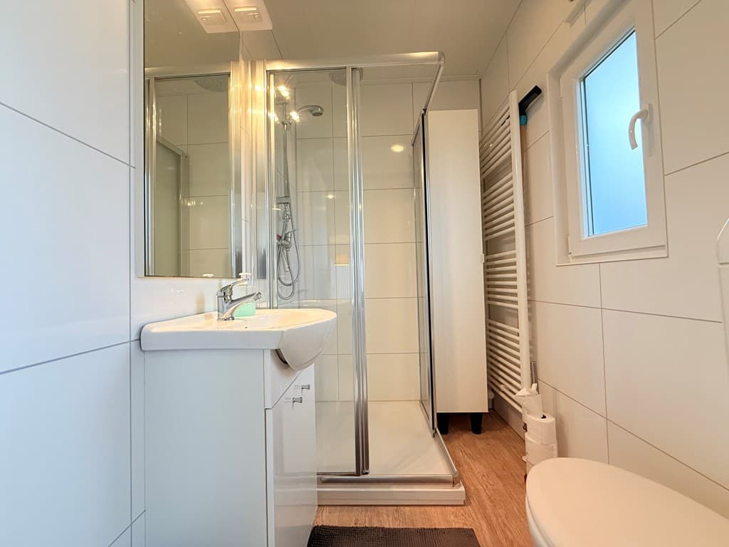 Moderne badkamer met douche, wastafel en toilet, voorzien van witte tegels en houten vloer.