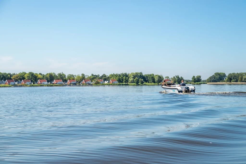 Uitzicht op het water met een boot en vakantiehuizen aan de oever in de verte, helder blauwe lucht.