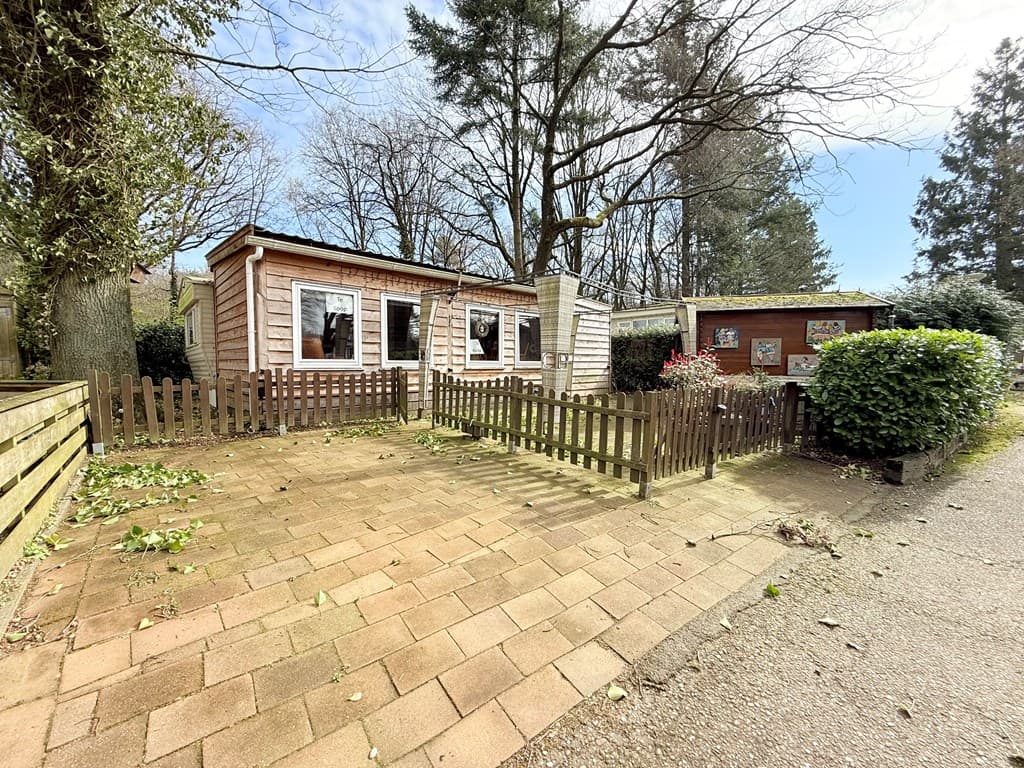 Buitenaanzicht van een houten woning met omheinde patio en omringende bomen bij Camping De Goudsberg in Lunteren