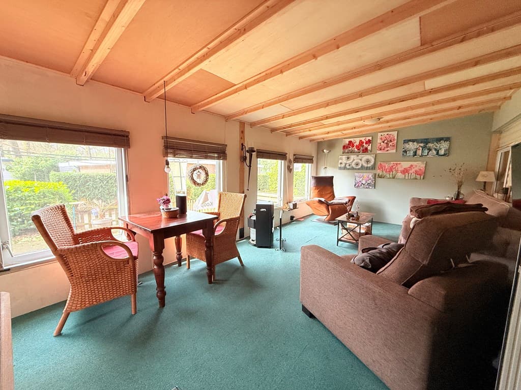 Lichte woonkamer met glazen wanden, houten plafond, meubels en schilderijen aan de muur