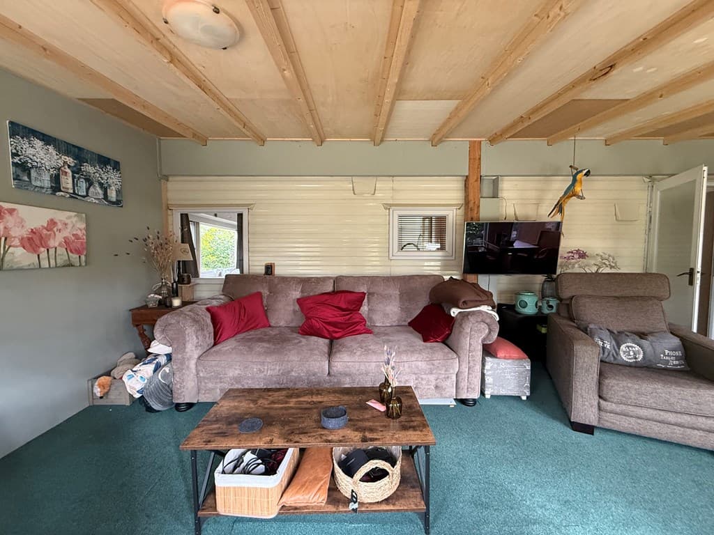 Gezellige woonkamer met een grijze bank, rode kussens, een houten salontafel en een fauteuil op een groene vloer.