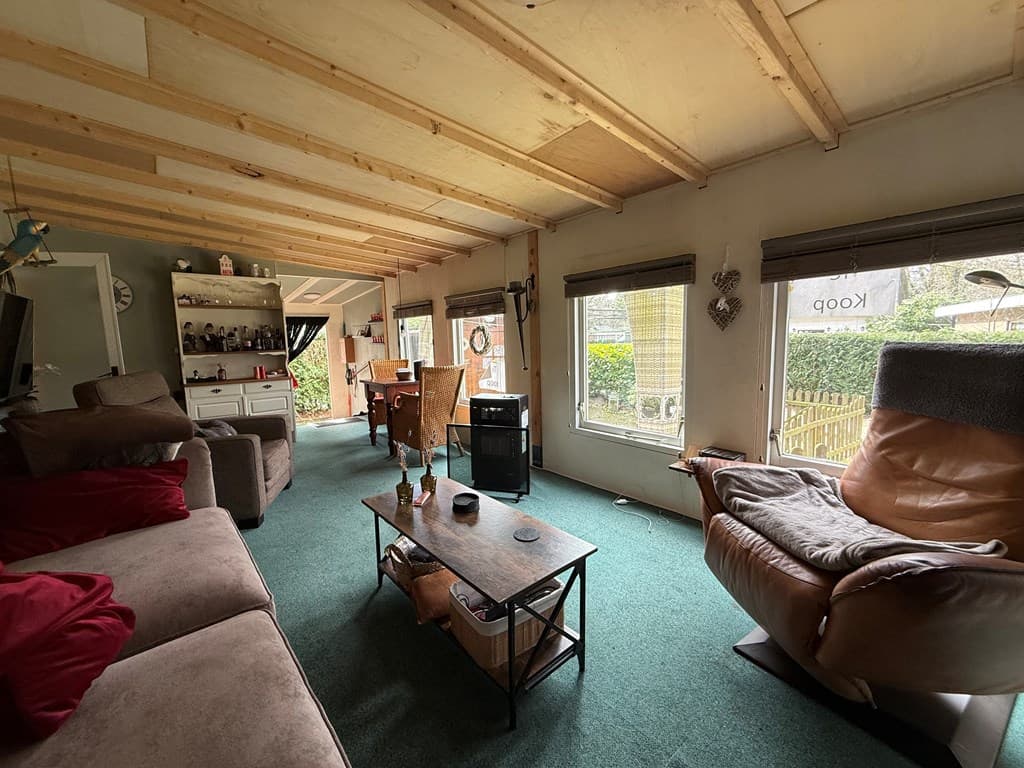 Interieur van een vakantiewoning met een zithoek, eetruimte en grote ramen met uitzicht op de tuin.