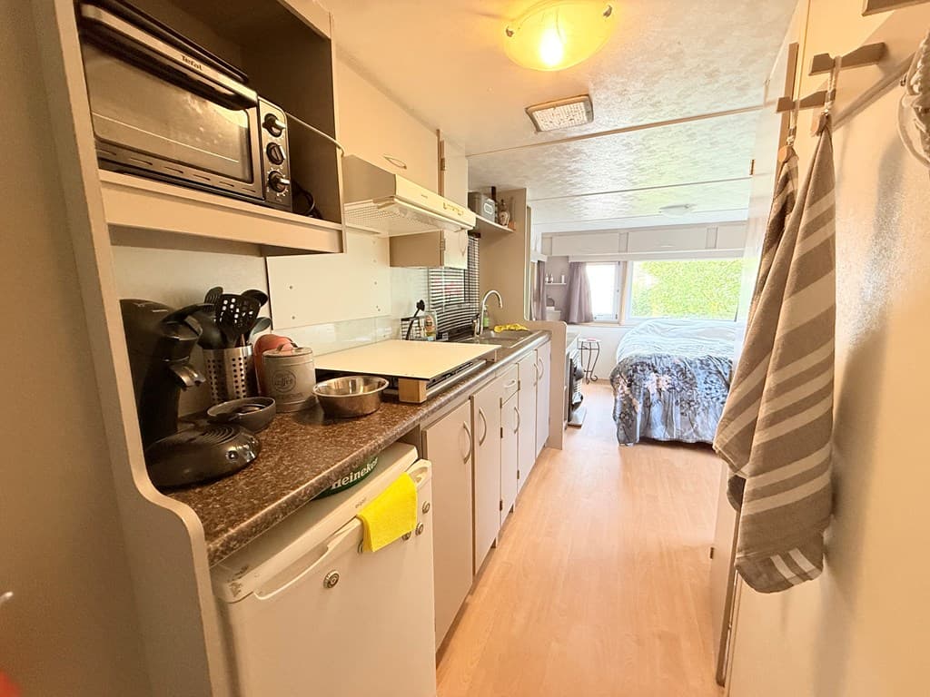 Keukenruimte met afwasbak, magnetron en koelkast, uitzicht op slaapkamer met tweepersoonsbed en raam naar buiten