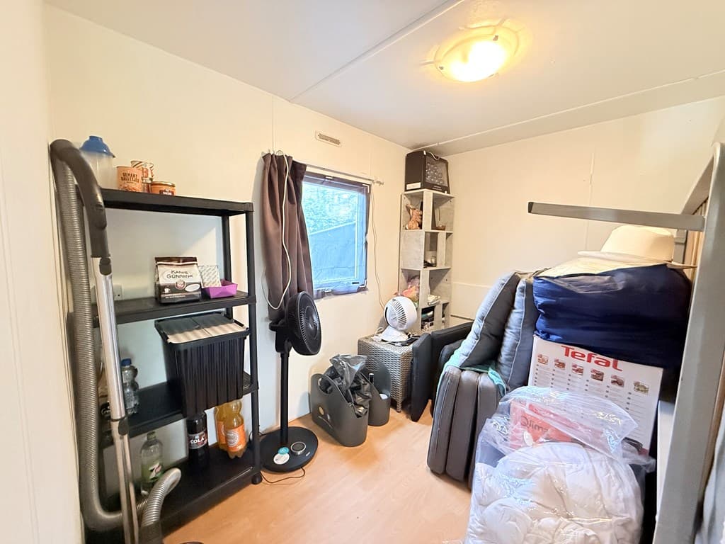 Klein wooninterieur met een boekenkast, ventilator en opgerolde dekens in een rustige, opgeruimde ruimte.
