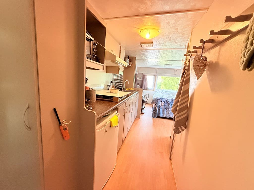 Ingericht interieur met gang, keuken met apparatuur en toegang tot slaapkamer met een bed en raam.