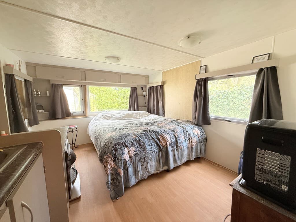 Ruime slaapkamer met een groot bed, gordijnen en een eenvoudig meubelstuk, gelegen in een lichte ruimte.