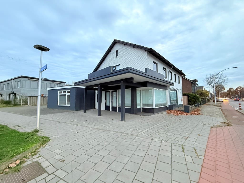 Hoekpand met een gedeeltelijk glazen gevel, gelegen op een klinkerstraat met gras en bomen ernaast