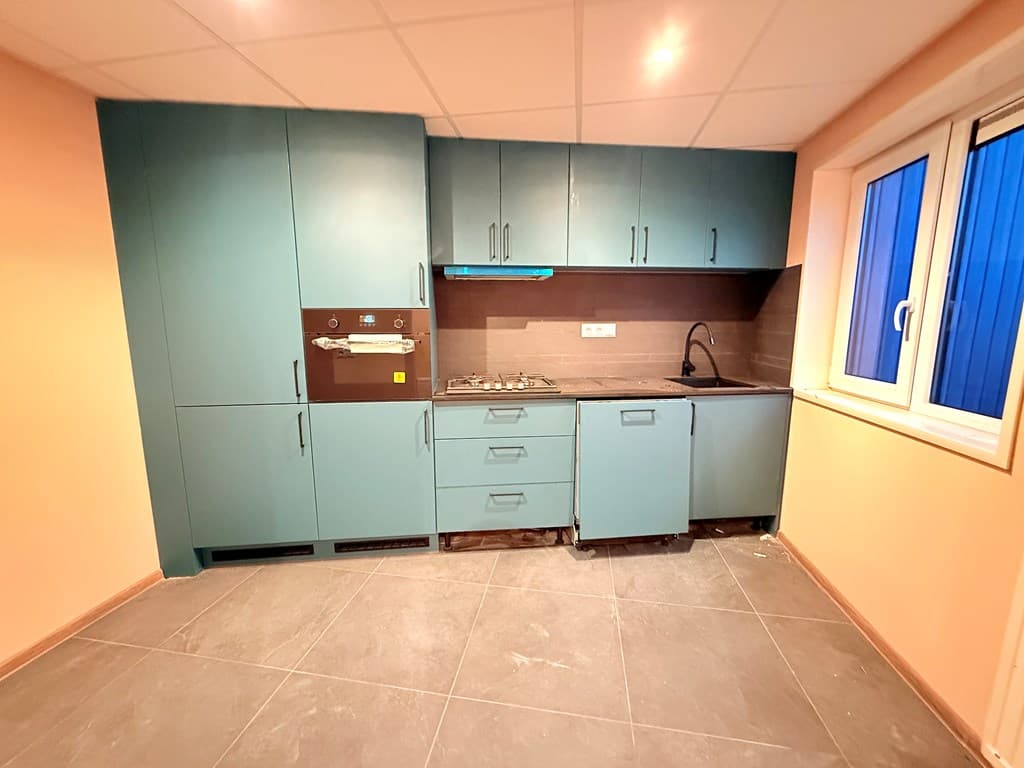 Gedeeltelijk ingerichte keuken met blauwe kasten, aanrecht en venster met uitzicht naar buiten.