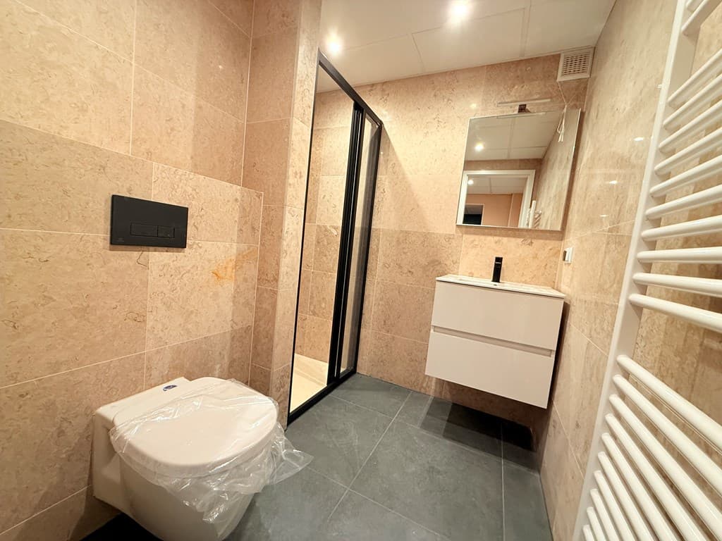 Moderne badkamer met natuurstenen wanden, inloopdouche, toilet en wastafel met opbergruimte.