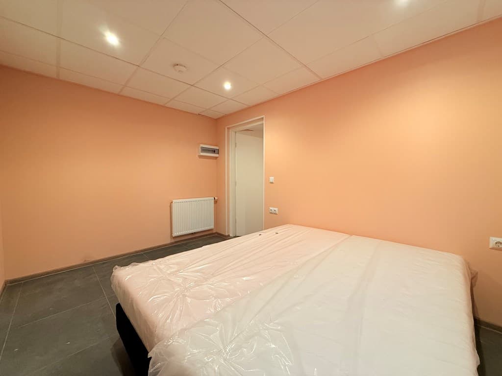 Slaapkamer met een oranje muur, een tweepersoonsbed en een radiator aan de muur.