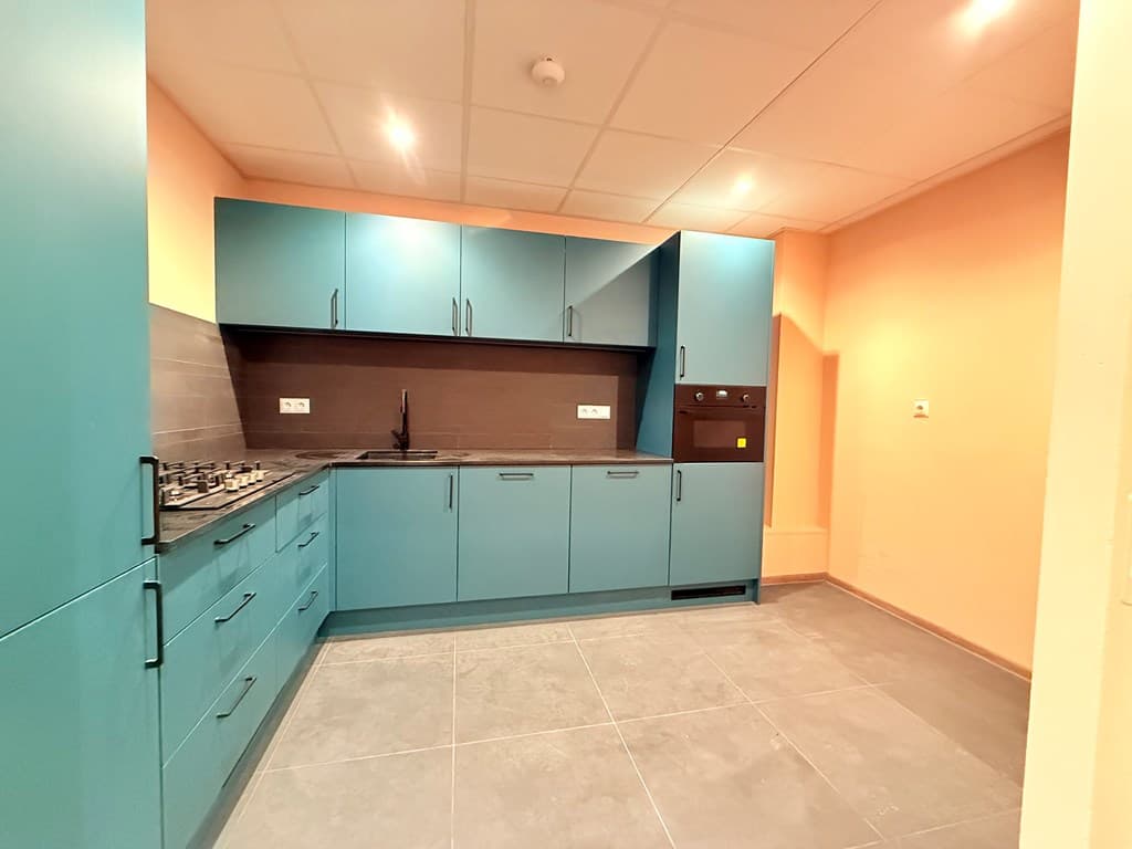Moderne keuken met turquoise kasten, donker werkblad en grijze vloertegels, met een wand in een warme kleur.