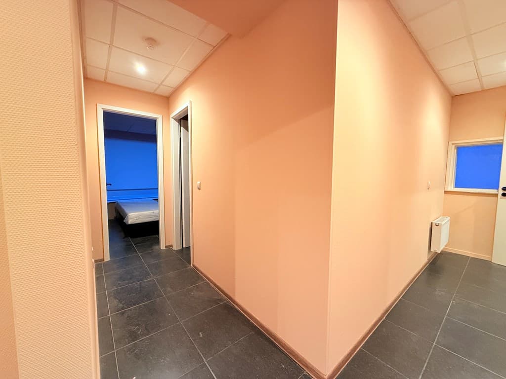 Lichtkleurige gang met een tegelvloer en toegang tot meerdere kamers, waaronder een slaapkamer aan het eind van de gang