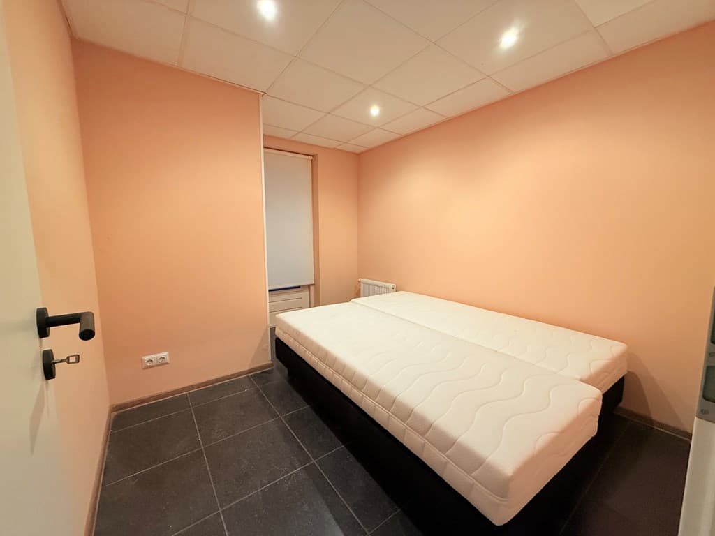 Slaapkamer met lichtgekleurde muren en twee verstelbare bedden zonder matrassen op een donkere tegelvloer