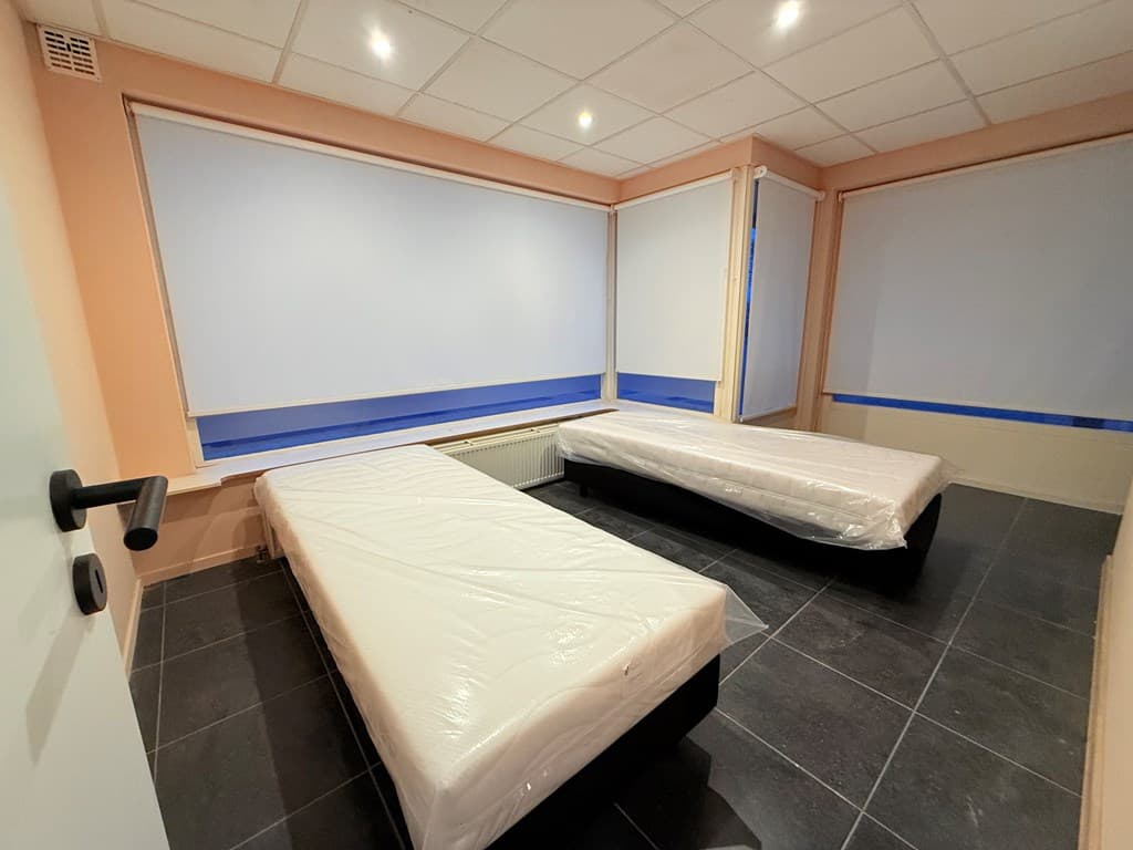 Slaapkamer met twee bedden, grote ramen met zonwering en tegels op de vloer.