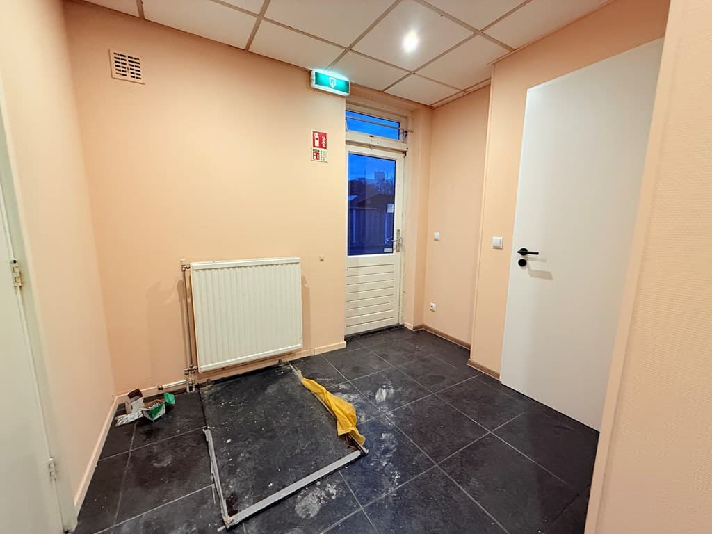 Entree met een lichtgekleurde muur, tegelvloer, verwarming en een deur naar buiten.