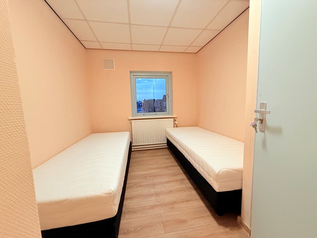 Kamer met twee eenpersoonsbedden, een raam en een lichte wandkleur in Hengelo.