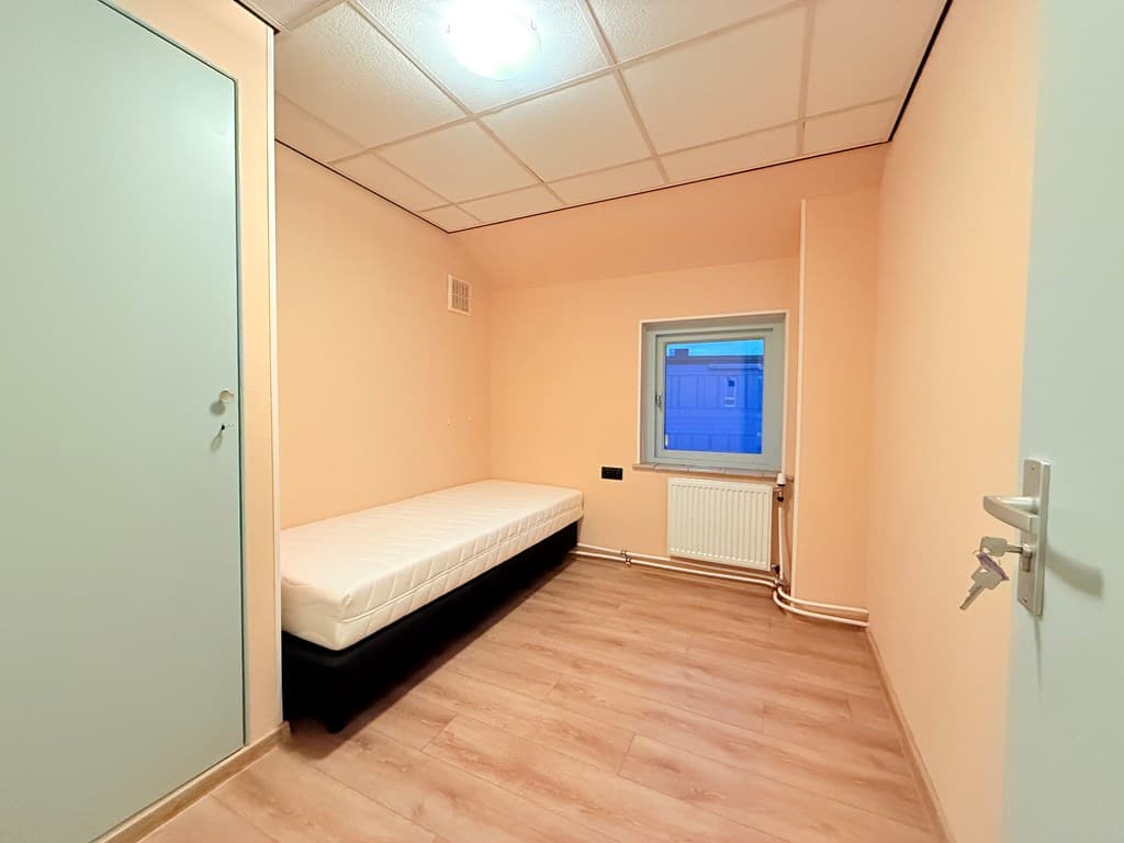 Kamer met een eenpersoonsbed, een raam en lichte wandkleuren, voorzien van een verwarming en laminaatvloer.