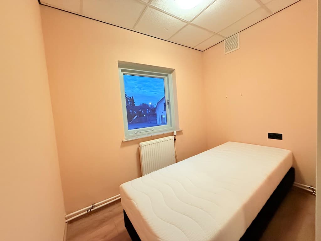 Kleine slaapkamer met een enkele bed en een raam met uitzicht op de buitenlucht.