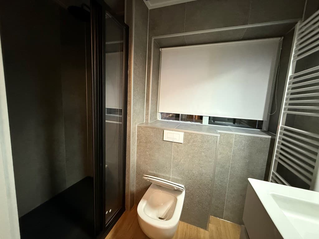 Badkamer met douchecabine, toilet, wastafel en een raam met verduistering.