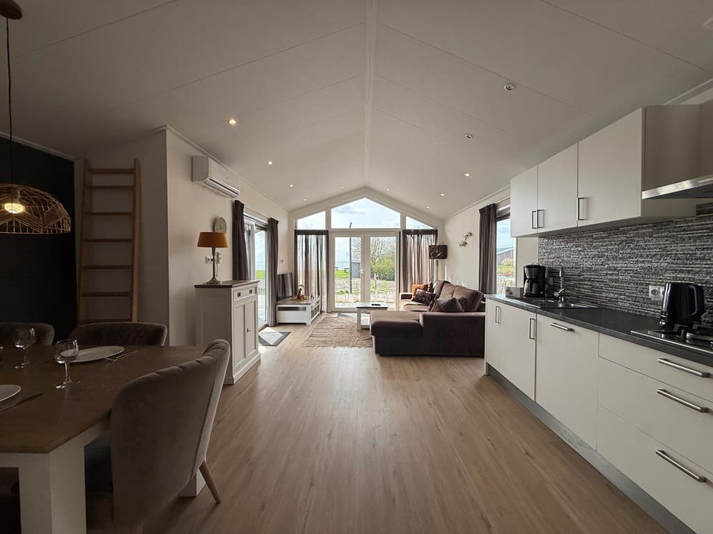 Moderne woonkamer met open keuken, grote ramen en uitzicht op het buitengebied, lichte inrichting met zithoek en eettafel