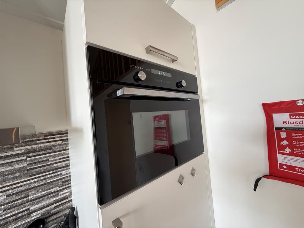 Zwarte inbouwoven met een modern design, geplaatst in een lichte keukenruimte met stenen wanddecoratie