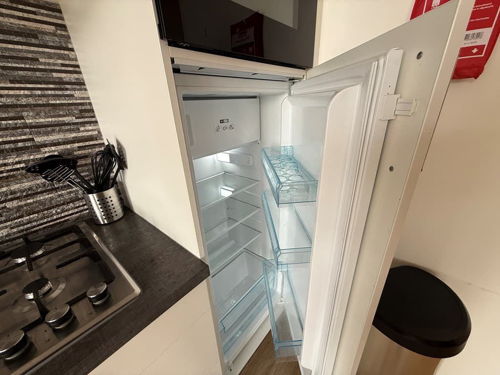 In de keuken is een open koelkast te zien met duidelijke schappen en een vriesvak bovenin.