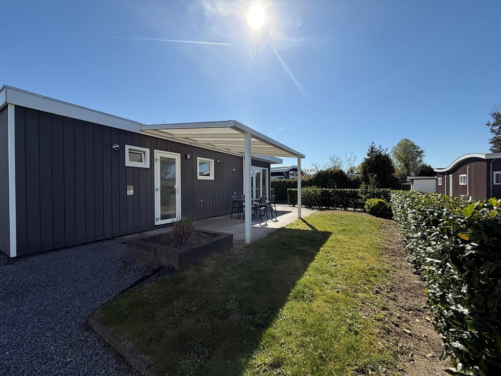 Moderne vakantiewoning met een terras en zithoek, omgeven door groene struiken en een blauwe lucht.