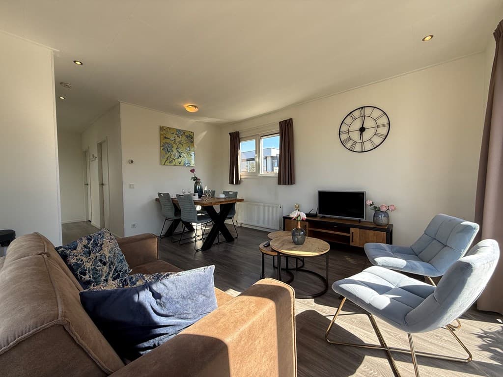 Moderne woonkamer met zitgedeelte, eettafel, tv en raam met natuurlijk licht in EuroParcs De Biesbosch, Dordrecht