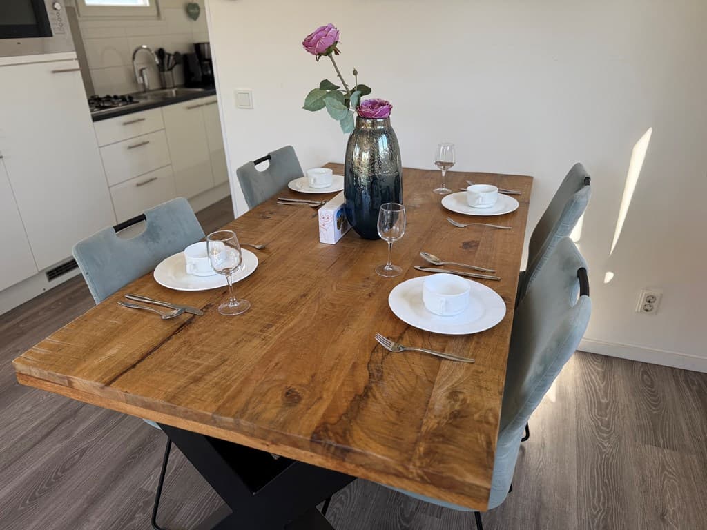 Eettafel met vier stoelen, servies en een vaas met rozen in een lichte ruimte met moderne keuken.