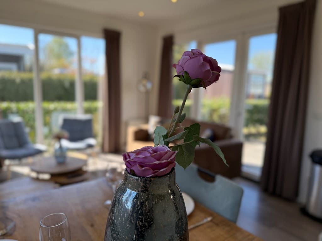 Eettafel met een vaas met rozen, zithoek met comfortabele stoelen en grote deuren naar de buitenruimte.