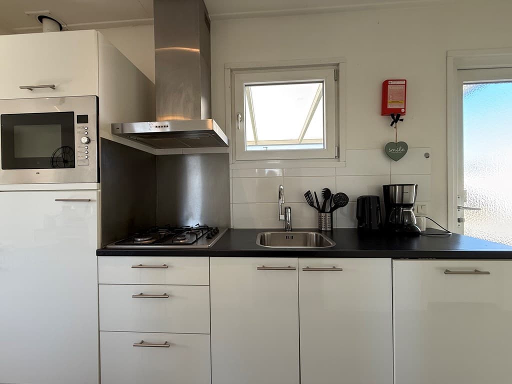 Moderne keuken met een gasfornuis, afzuigkap, spoelbak en apparatuur zoals een magnetron en koffiezetapparaat.