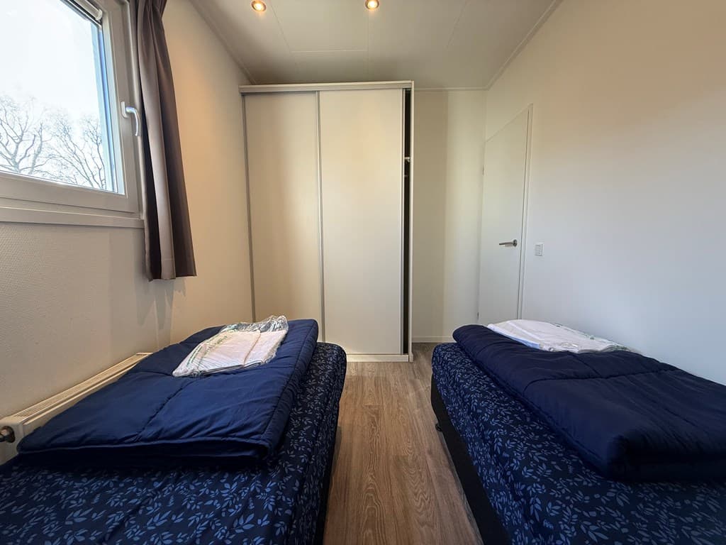 Slaapkamer met twee eenpersoonsbedden en een kast, raam met lichtinval en neutrale wanden.