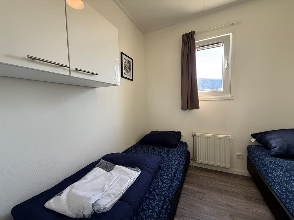 Slaapkamer met twee eenpersoonsbedden, raam met gordijn en muurkast met witte planken.
