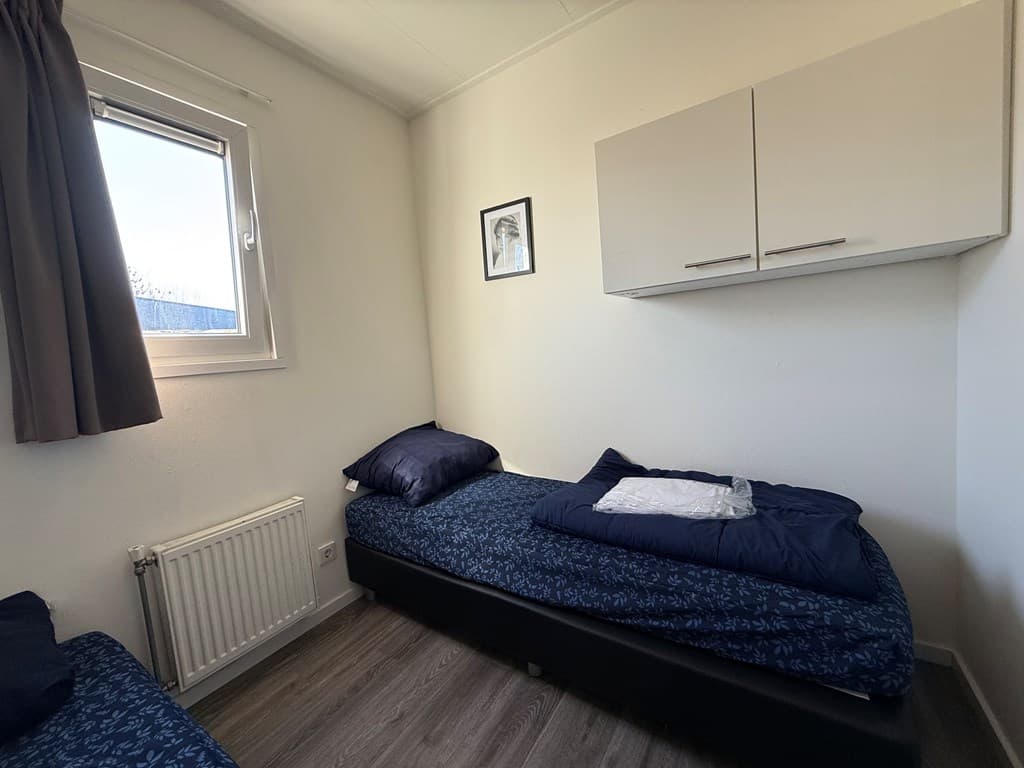 Slaapkamer met twee eenpersoonsbedden, een raam en een wandkast boven de bedden.