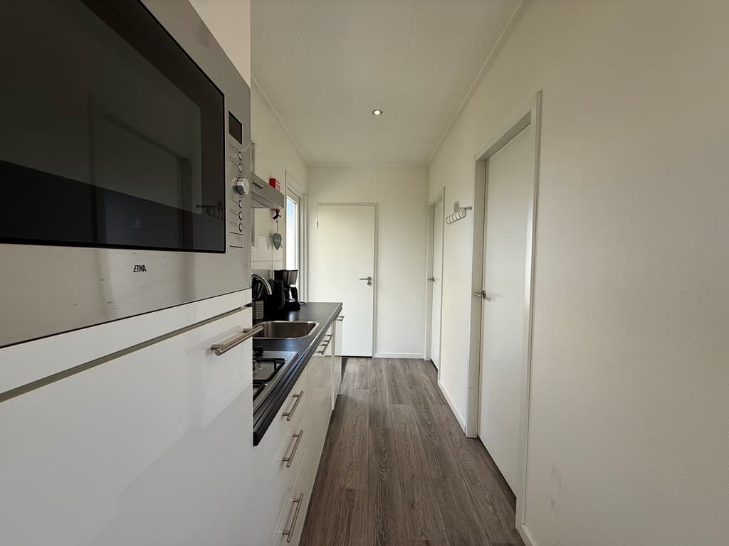 Keuken met moderne afwerkingen, waaronder een oven, fornuis en apparatuur, lichte muren en toegang tot een deur aan het einde