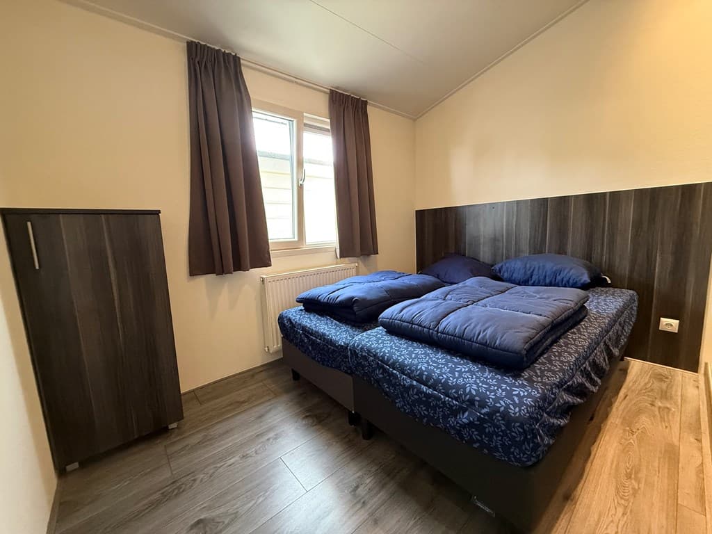 Slaapkamer met een tweepersoonsbed, kast en ramen met gordijnen in EuroParcs De Biesbosch, Dordrecht