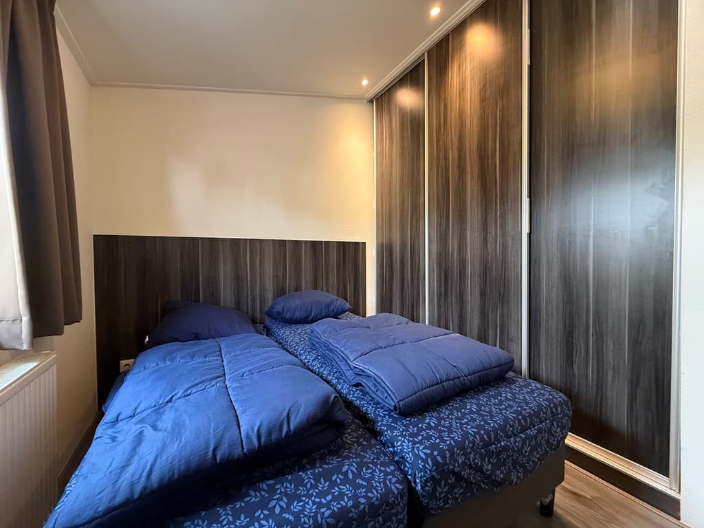 Slaapkamer met twee eenpersoonsbedden en een ruime, donkere kastenwand.