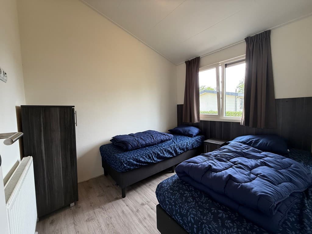 Slaapkamer met twee eenpersoonsbedden, raam met uitzicht en een kast tegen de wand.
