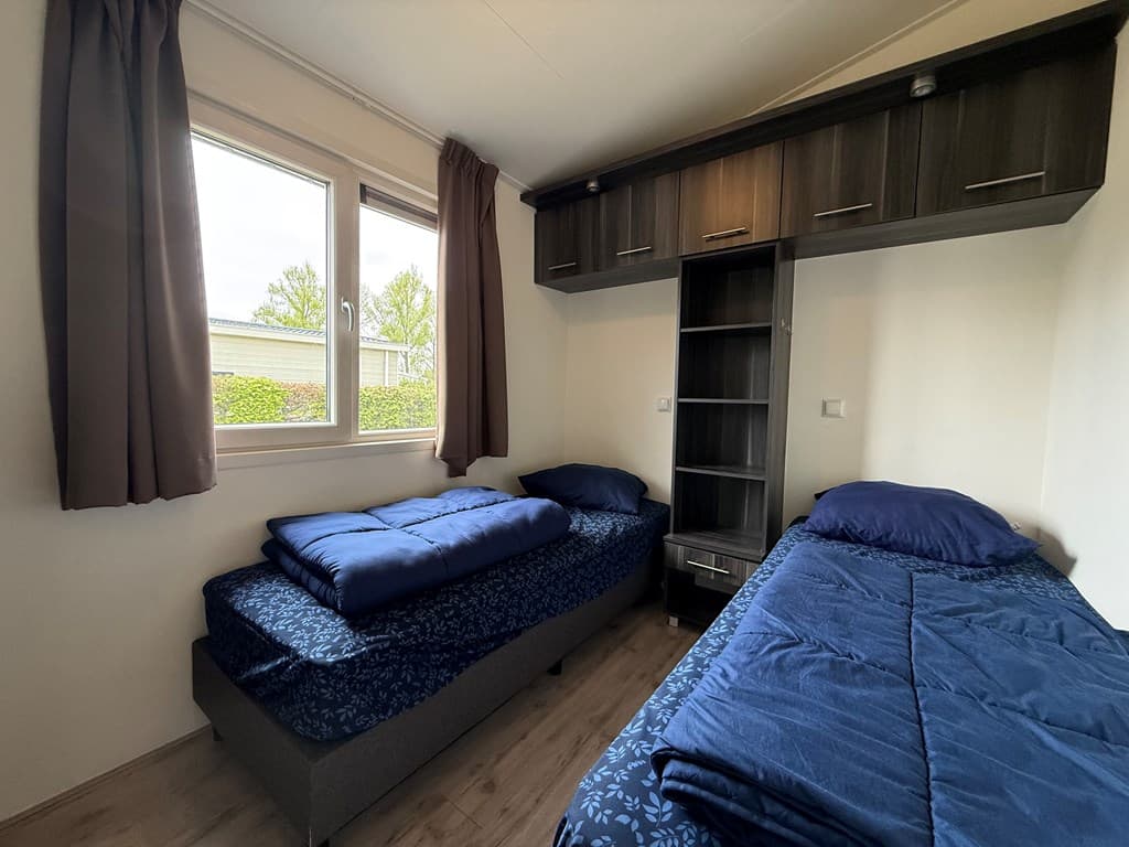 Slaapkamer met twee eenpersoonsbedden, kast en ramen met uitzicht op groen bij EuroParcs De Biesbosch.