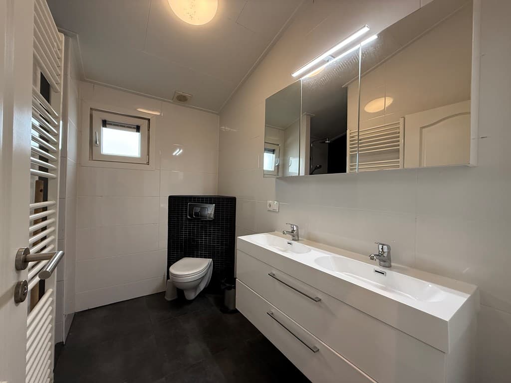 Moderne badkamer met dubbele wastafel, toilet, grote spiegels en verlichte wandpanelen in neutrale kleuren